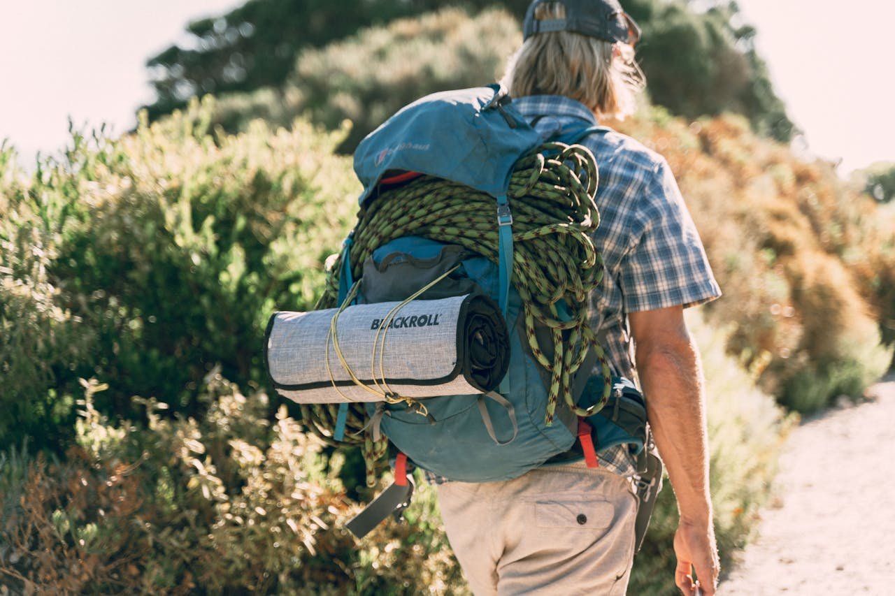 A man with hiking gear walks through a sunlit trail, showcasing outdoor adventure.